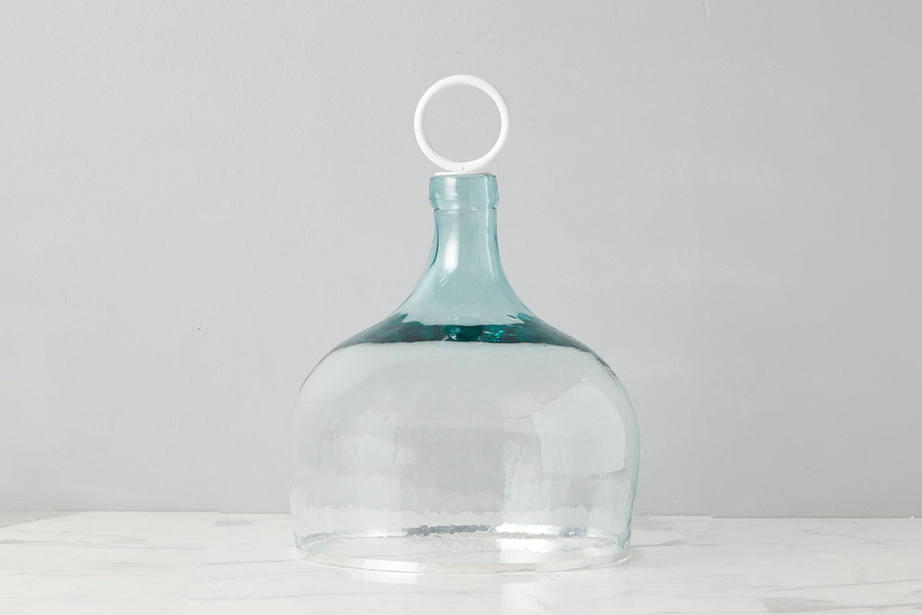 Bianca Recycle Glass Mouth-Blown Cloche by etúHOME. The silhouette of a classic wine bottle demijoh with white iron handle.