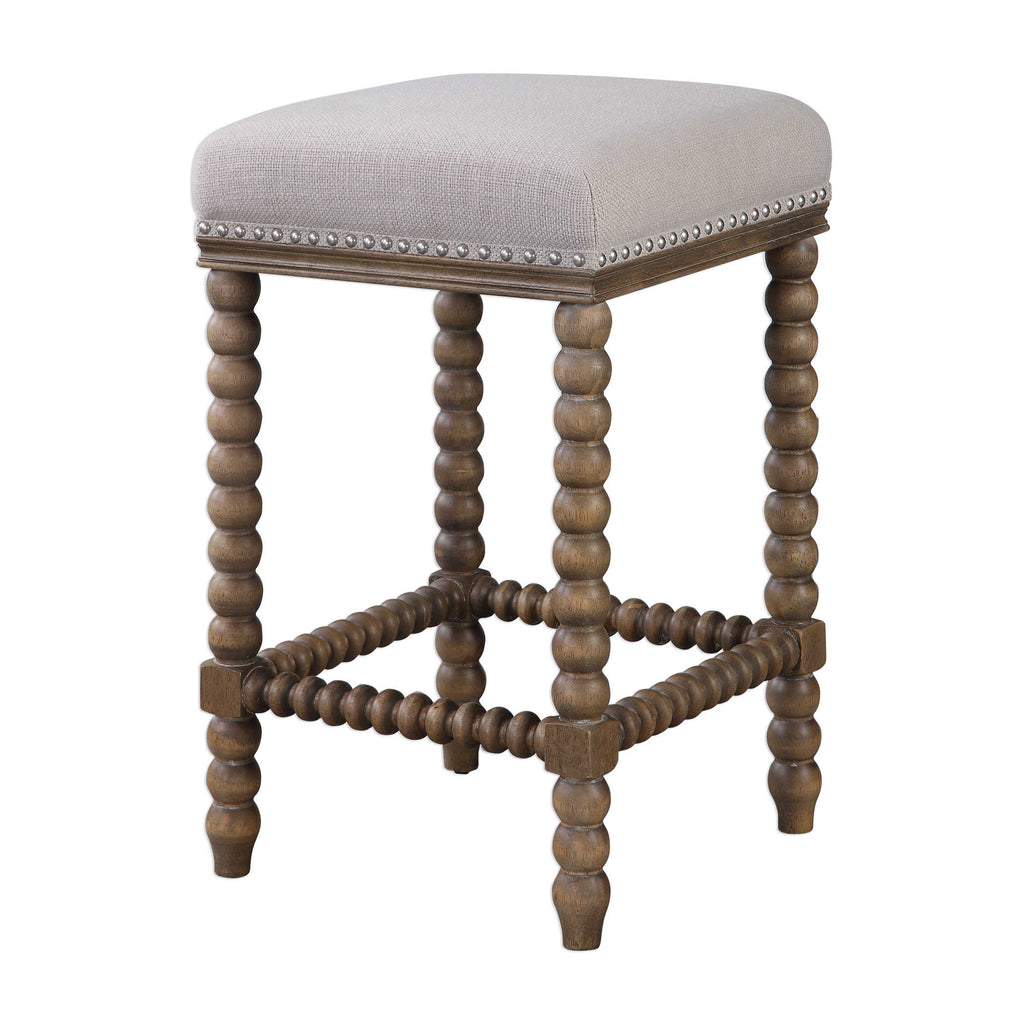 Pryce Counter Stool by Uttermost featuring spindle turned legs and carved trim finished in a light walnut stain. Plush seat is tailored in a soft ivory linen blend fabric accented with brushed nickel nail head trim. Seat height is 26".