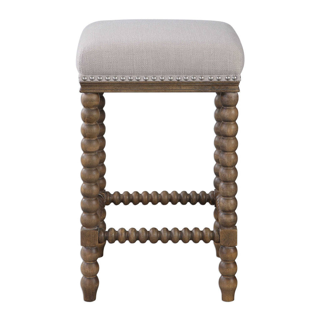 Pryce Counter Stool by Uttermost featuring spindle turned legs and carved trim finished in a light walnut stain. Plush seat is tailored in a soft ivory linen blend fabric accented with brushed nickel nail head trim. Seat height is 26".